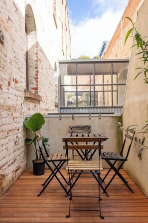 Een terras met een houten tafel en stoelen, een plant in pot en uitzicht door een raam.