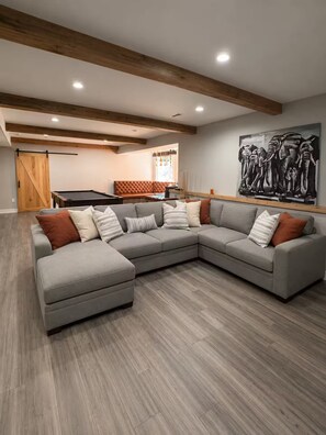 A modern living room with a sectional sofa, wooden beams on the ceiling, a pool table, and a large abstract painting. - Spacious Family Retreat Near Ann Arbor & U-M (Ypsilanti)