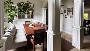 A dining area with a wooden table and chairs, a built-in bench, and a hanging plant. - Spacious Family Retreat Near Ann Arbor & U-M (Ypsilanti)