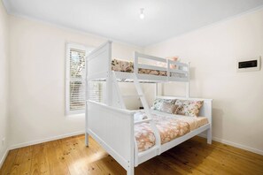 A bunk bed with a white frame and floral bedding, a window with blinds, and a light switch on the wall. - Cabinesque Comfort A Refreshing Beachside Retreat (Barwon Heads)