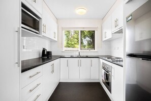 A modern kitchen with white cabinets, a black countertop, and stainless steel appliances. - Cabinesque Comfort A Refreshing Beachside Retreat (Barwon Heads)