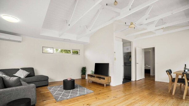 Uma sala de estar moderna com um sofá cinzento, uma mesa de centro preta e uma mesa de jantar de madeira com cadeiras.