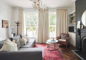 A living room with a grey sofa, a red armchair, a coffee table, and a fireplace. - Nicholson Nook Parkside Stay near Dining and Culture (Fitzroy)