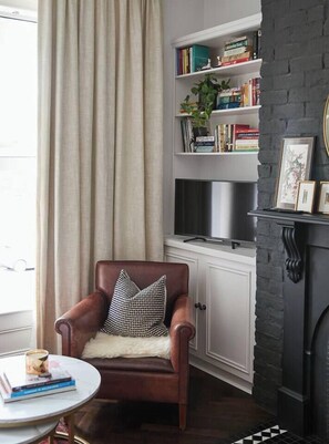 A cozy living room with a leather armchair, a bookshelf, a fireplace, and a television. - Nicholson Nook Parkside Stay near Dining and Culture (Fitzroy)