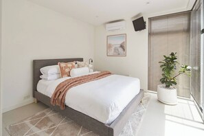 A modern bedroom with a bed, a potted plant, and a window with blinds. - Swanston Sands Sophisticated Comfort by the Beach (Geelong)