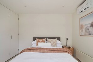 A bedroom with a bed, nightstand, and wall-mounted air conditioning unit. - Swanston Sands Sophisticated Comfort by the Beach (Geelong)