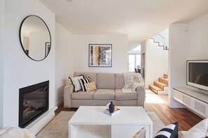 A modern living room with a sofa, a coffee table, a fireplace, a television, and a staircase leading to another level. - Swanston Sands Sophisticated Comfort by the Beach (Geelong)