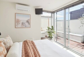 A bedroom with a large bed, a mounted TV, a window, and a balcony with a plant. - Swanston Sands Sophisticated Comfort by the Beach (Geelong)