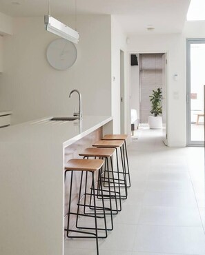 A modern kitchen with a bar area, a clock on the wall, and a potted plant in the background. - Swanston Sands Sophisticated Comfort by the Beach (Geelong)