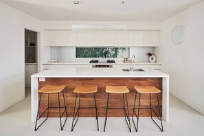 A modern kitchen with a central island, bar stools, and a clock on the wall. - Swanston Sands Sophisticated Comfort by the Beach (Geelong)