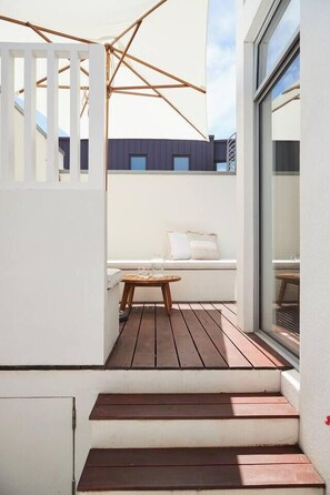 A wooden deck with a white bench and a small table, leading to a white wall with a window. - Swanston Sands Sophisticated Comfort by the Beach (Geelong)