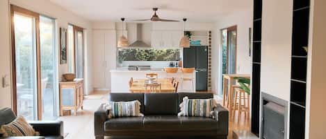 A modern living room with a sofa, a fireplace, and a dining area with a kitchen in the background.