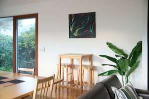 Ein Zimmer mit einem Holzespeiseplatz, Stühlen, einem grauen Sofa, einem Stehtisch und einer großen Grünpflanze.