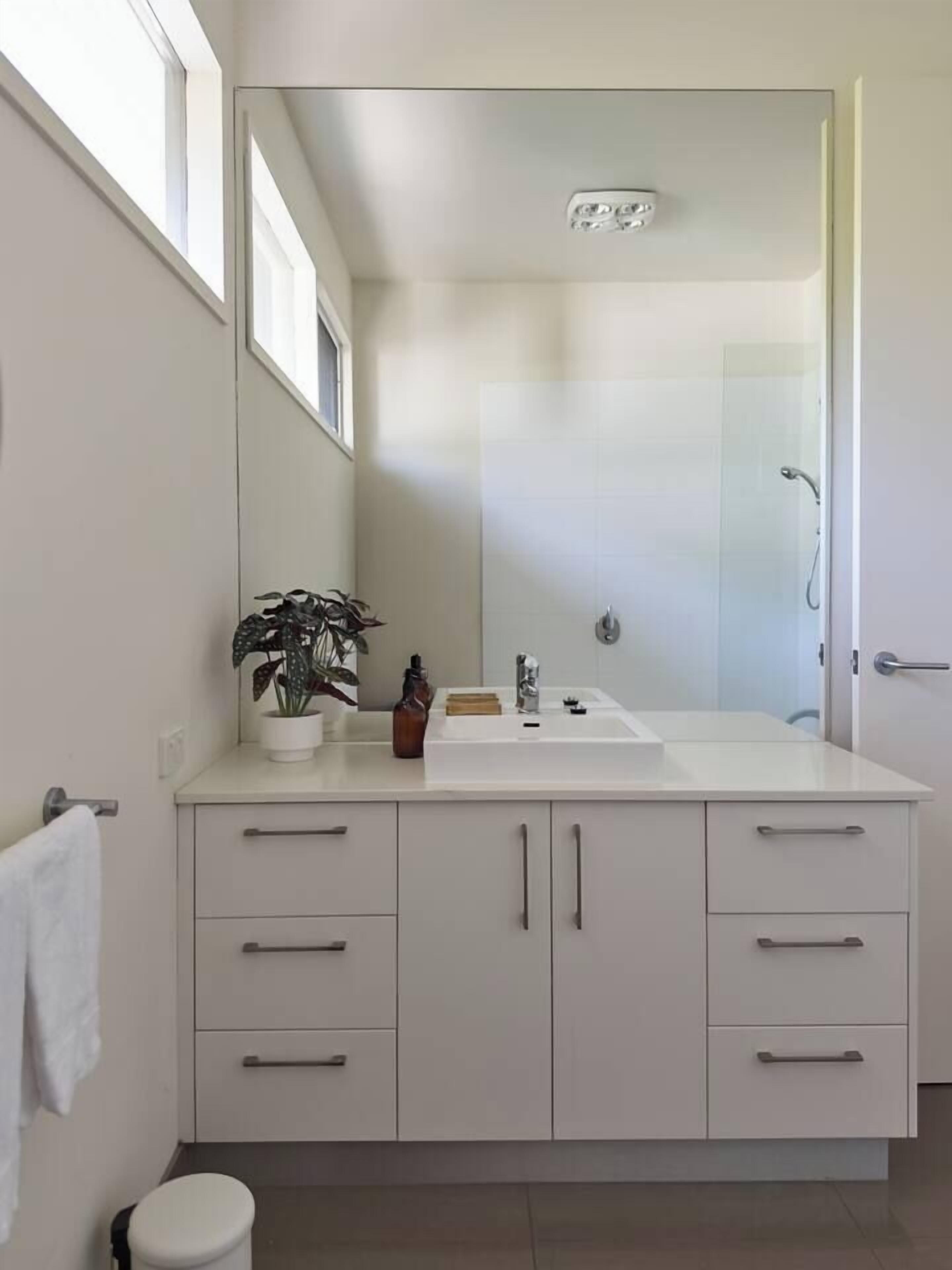 Une salle de bain moderne avec un meuble-lavabo blanc, un miroir, un lavabo et un espace douche.