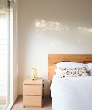 A bedroom with a wooden headboard, a bedside table with a lamp, and a bed with patterned pillows. - The Garden Escape Slow Living by Beach and Wildlife (Saint Leonards)