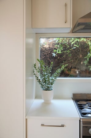 Eine Küche mit weißer Arbeitsplatte, einem weißen Herd und einem Fenster mit Blick auf Grünflächen.