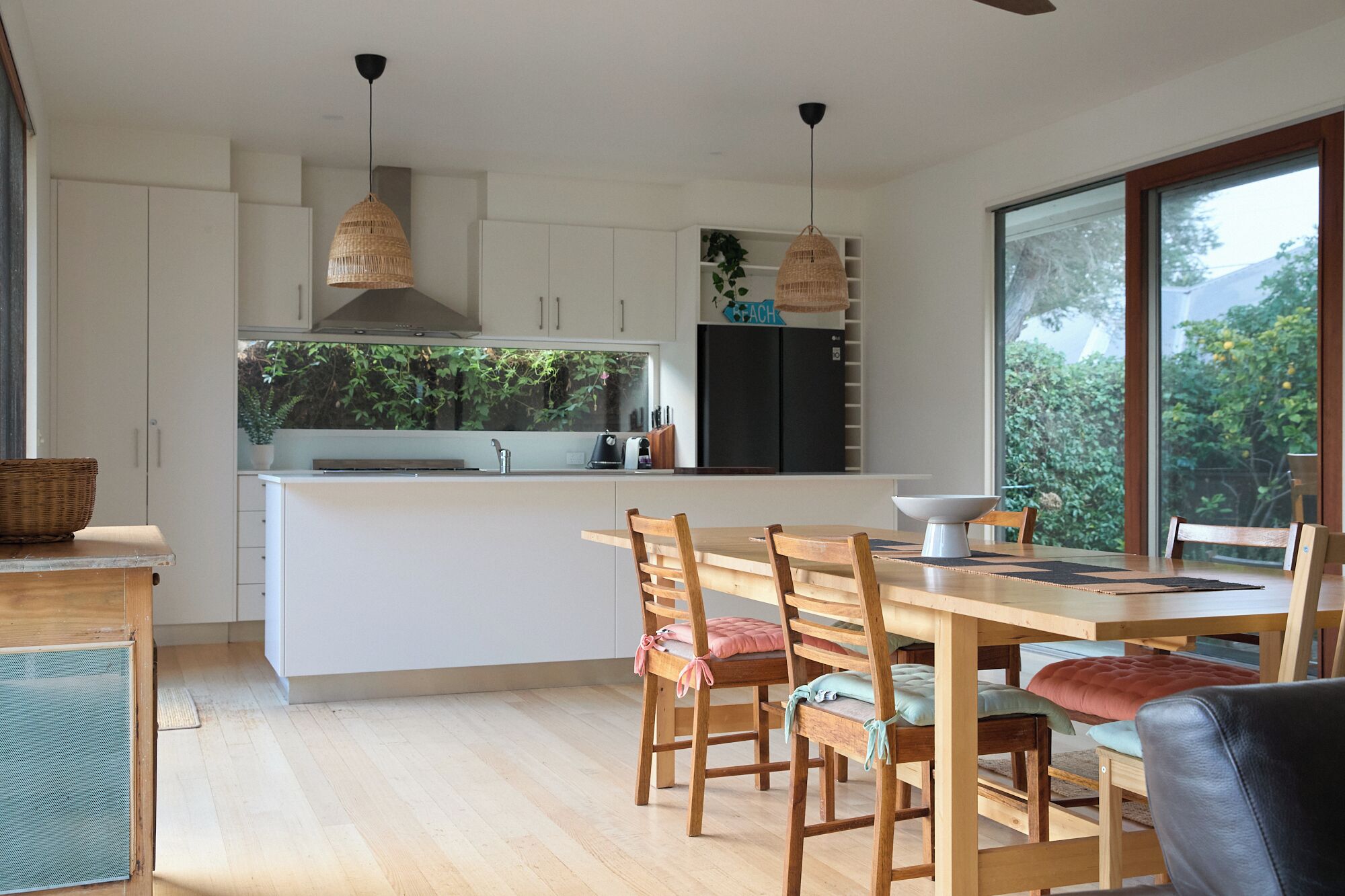 Una cocina moderna con armarios blancos, una isla central y un comedor con sillas y una mesa de madera.