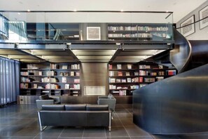 Eine moderne Bibliothek mit einer gebogenen Rezeption, zahlreichen Bücherregalen und einer gemütlichen Sitzecke.