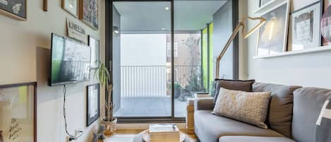 A living room with a sofa, a television, and a bookshelf. There is a sliding glass door leading to an outdoor area.