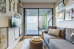 Ein Wohnzimmer mit einer Couch, einem Fernseher und einem Bücherregal. Eine Glastür öffnet sich zu einem Außenbereich.