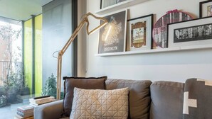 A modern living room with a sofa, a floor lamp, and framed pictures on the wall. - Urban Escape on Smith Street w Balcony and Parking (Collingwood)