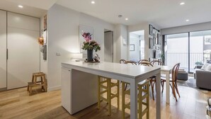 A modern kitchen with a central island, wooden chairs, and a dining table. - Urban Escape on Smith Street w Balcony and Parking (Collingwood)