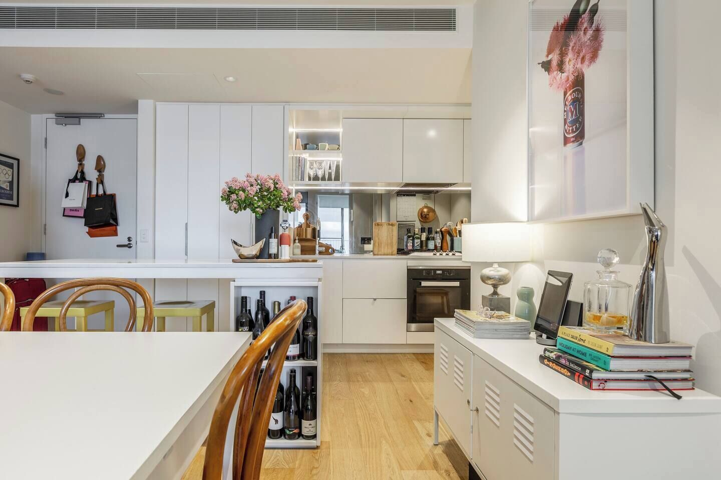 Una cocina moderna con armarios blancos, un comedor con sillas de madera y una pequeña isla con un florero.