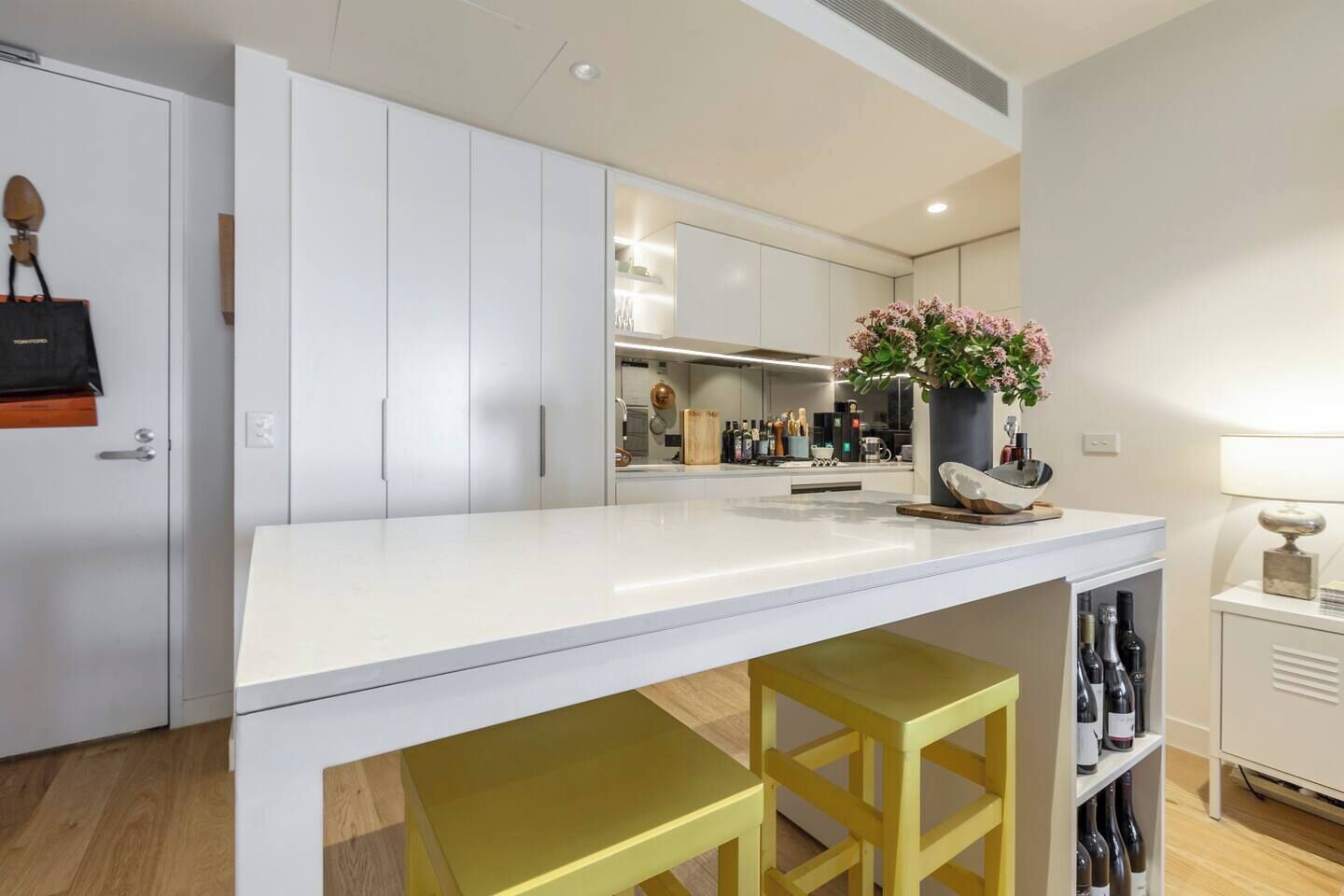 A modern kitchen with white cabinets, a central island with stools, and a wine rack.