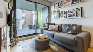 A modern living room with a grey sofa, a coffee table, and a bookshelf with framed pictures. - Urban Escape on Smith Street w Balcony and Parking (Collingwood)