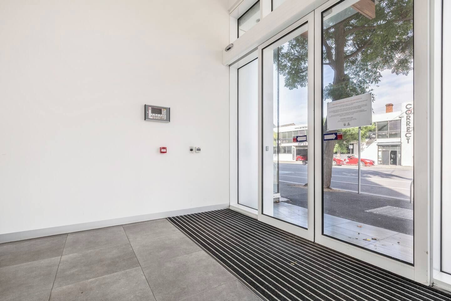 A clean, modern entrance with a glass door, a fire alarm, and a sign indicating the direction to the parking area.