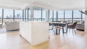 A modern kitchen with large windows, a dining area with a wooden table and chairs, and a city view. - The Fawn Relish in Sub Penthouse Panorama (North Melbourne)