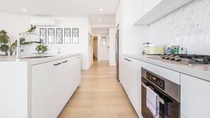 A modern kitchen with white cabinetry, a stainless steel range, and a wooden floor. - The Fawn Relish in Sub Penthouse Panorama (North Melbourne)