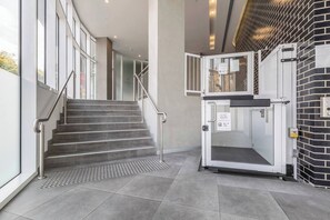 A modern hotel lobby with a staircase, a glass elevator, and a metal security gate. - The Fawn Relish in Sub Penthouse Panorama (North Melbourne)