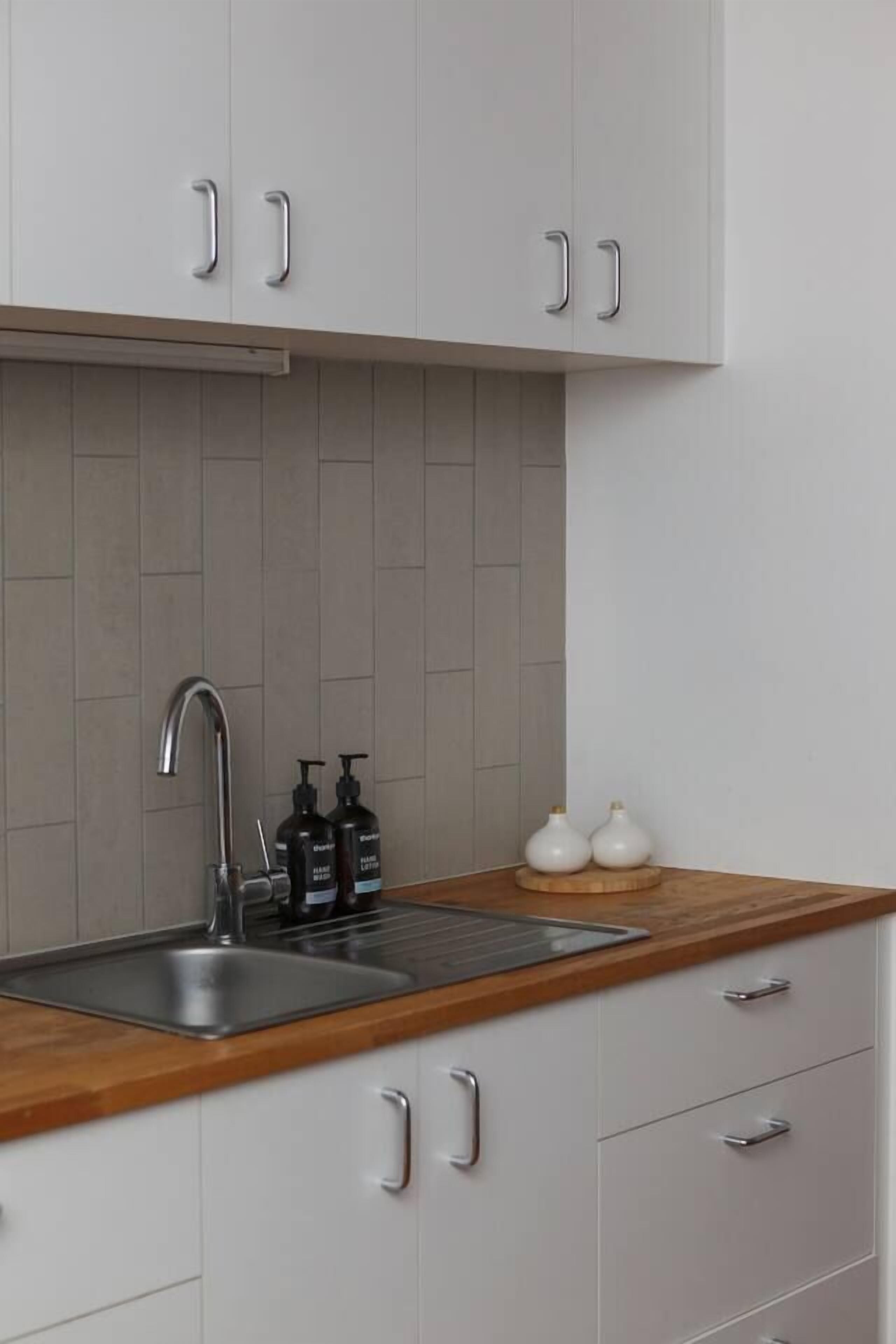 A kitchen with white cabinets, a wooden countertop, a stainless steel sink, and two white ceramic vases on the counter.