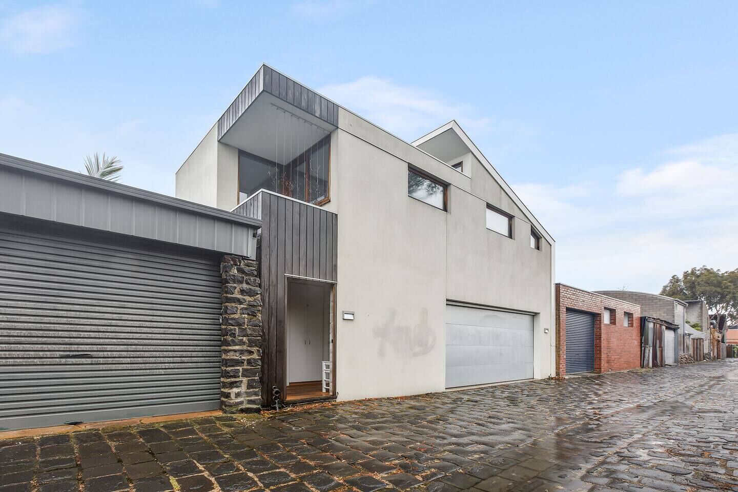 Un bâtiment moderne à deux étages, doté d’un garage, d’un mur en pierre et situé sur une rue pavée.