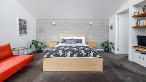 Quarto moderno com cama, sofá vermelho, ventilador de teto, estante e relógio fixado na parede.