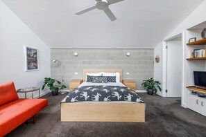 Ein modernes Schlafzimmer mit einem Bett, einem roten Sofa, einem Deckenventilator, einem Bücherregal und einer Wanduhr.