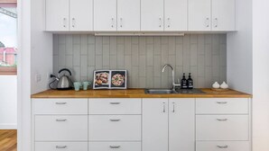 Uma cozinha moderna com armários brancos, bancada de madeira, chaleira, livro de receitas, pia e duas embalagens de sabonete líquido para as mãos.