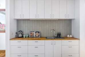 Eine moderne Küche mit weißen Schränken, einer Holz Arbeitsplatte, einem Wasserkocher, einem Kochbuch, einer Spüle und zwei Flaschen Handseife.