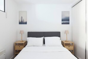 Ein minimalistisch eingerichtetes Hotelzimmer mit einem Bett, zwei Nachttischen und zwei Wandlampen.