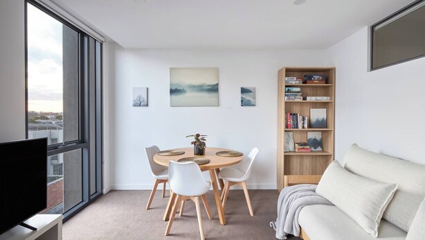 A modern living room with a dining area, a sofa, a bookshelf, and a TV. - Northside Rendezvous A Stylish Couples Hideaway (Brunswick East)