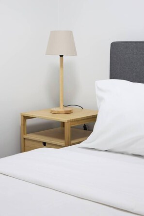 Ein Bett mit einem weißen Kissen und einem Nachttisch aus Holz mit einer Lampe.