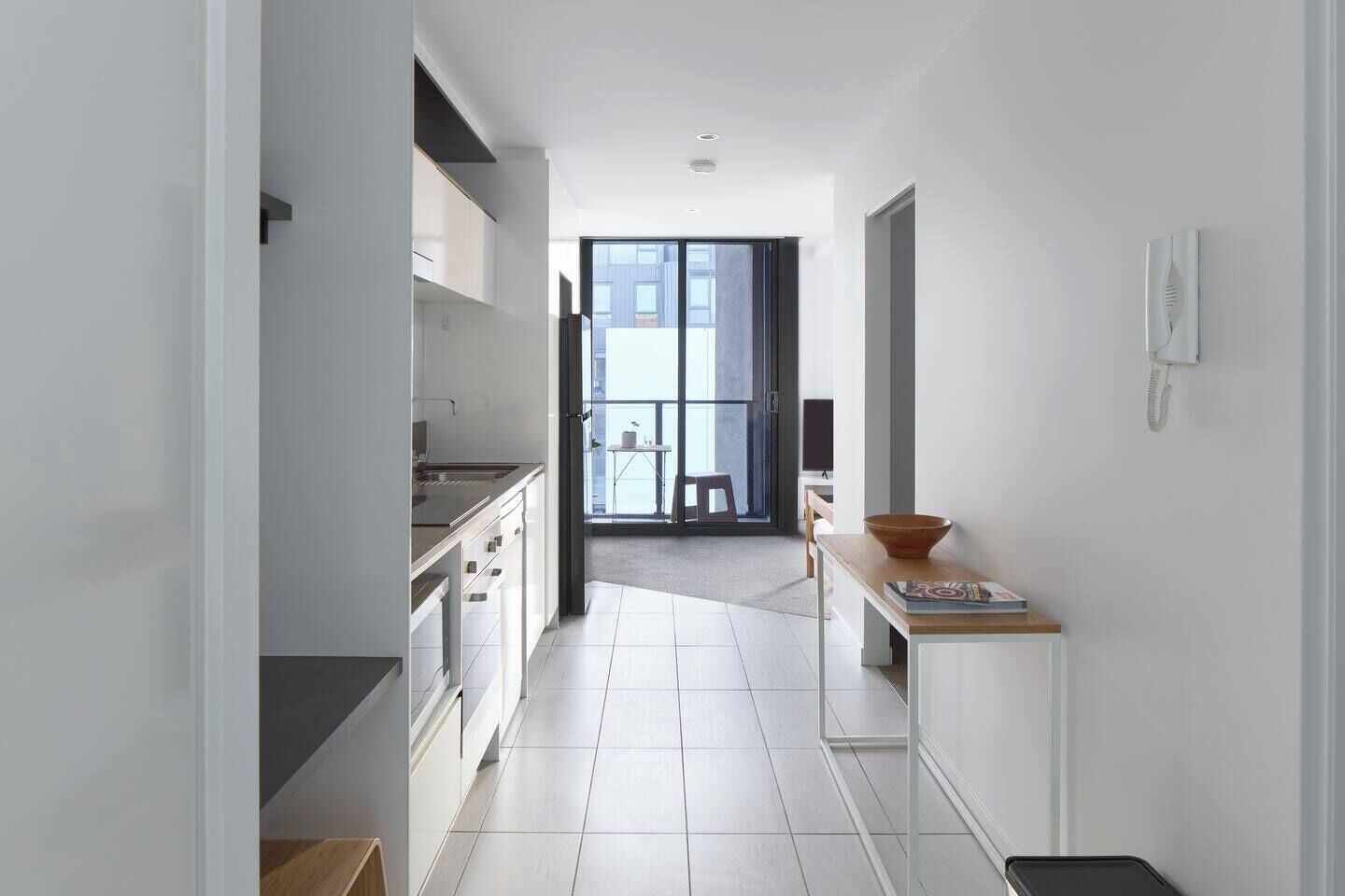 A modern kitchen with white cabinets, a wooden countertop, and a view to an outdoor balcony.
