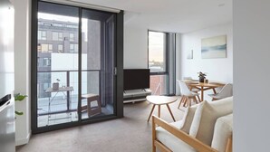 A modern apartment with a balcony, a dining area, and a living room with a sofa and TV. - Northside Rendezvous A Stylish Couples Hideaway (Brunswick East)
