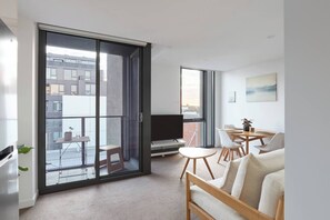 Ein modernes Apartment mit Balkon, Essbereich und Wohnzimmer mit Sofa und Fernseher.