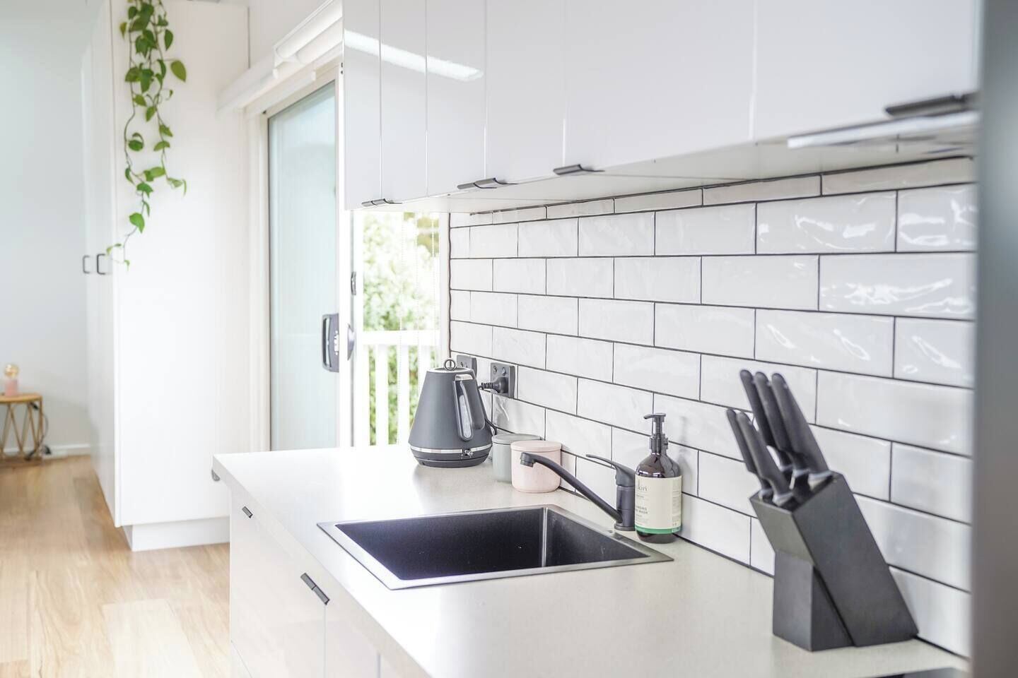 Une cuisine moderne avec des meubles blancs, une bouilloire noire, une machine à café et un bloc à couteaux.