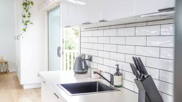 Une cuisine moderne avec des meubles blancs, une bouilloire noire, une machine à café et un bloc à couteaux.