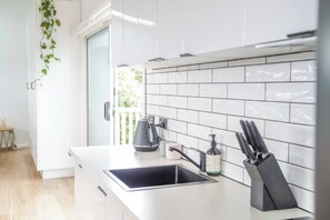 Une cuisine moderne avec des meubles blancs, une bouilloire noire, une machine à café et un bloc à couteaux.