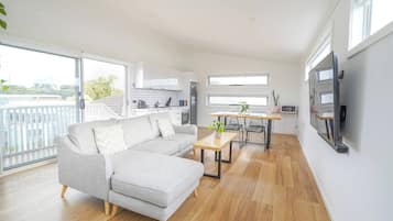 A modern living room with a grey sectional sofa, a wooden dining table with two chairs, and a kitchen in the background.