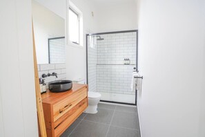 Et moderne badeværelse med et træskab, en sort vask, et hvidt toilet og en brusekabine med glasvægge.